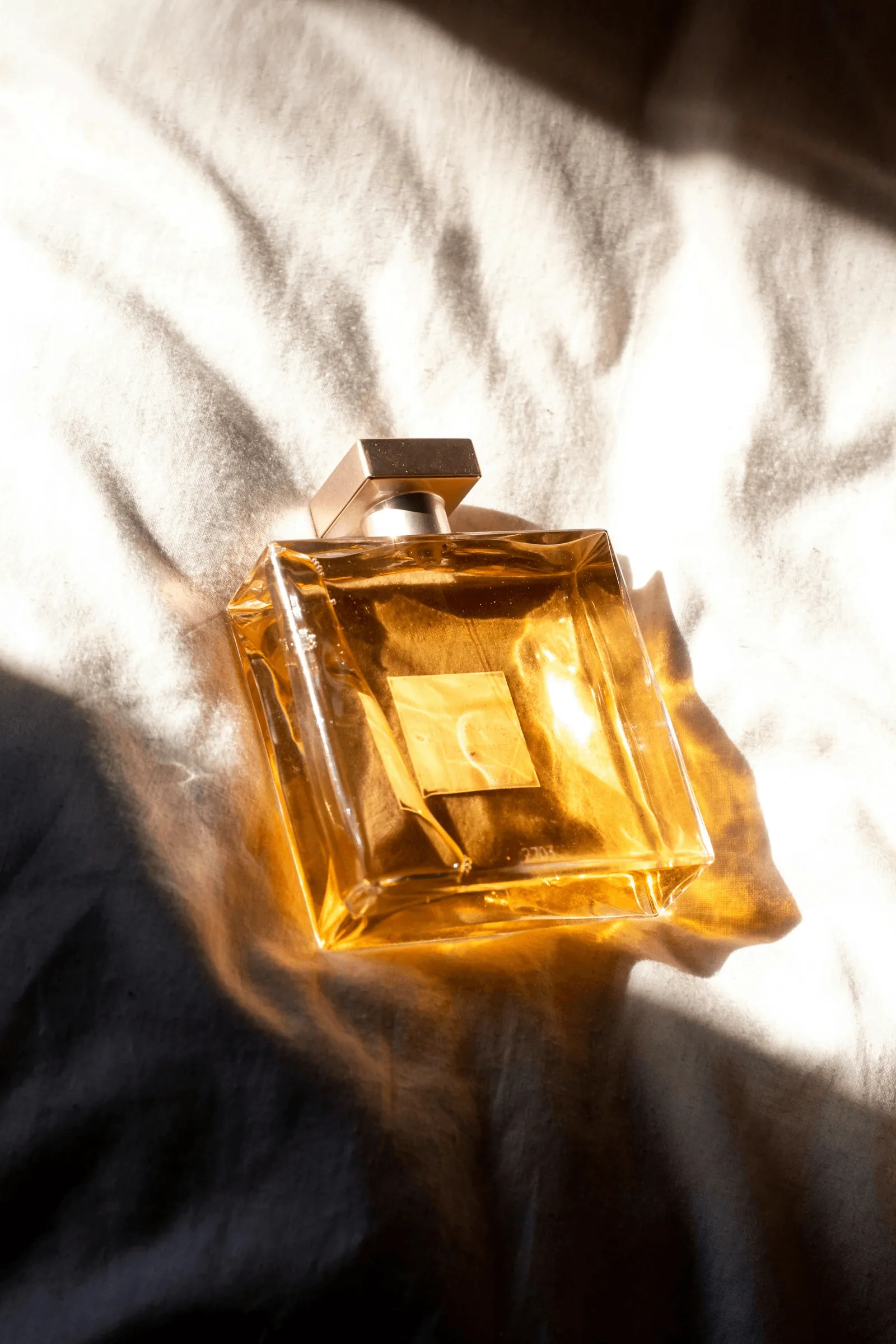 A gold Blushene flacon resting in sunlight on cream linen